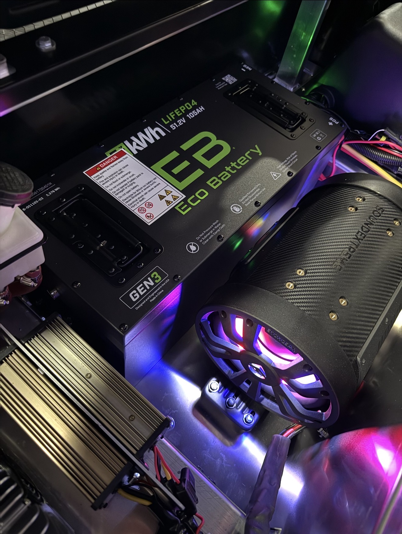 Installed EcoBattery lithium battery beside an illuminated EcoXGear subwoofer