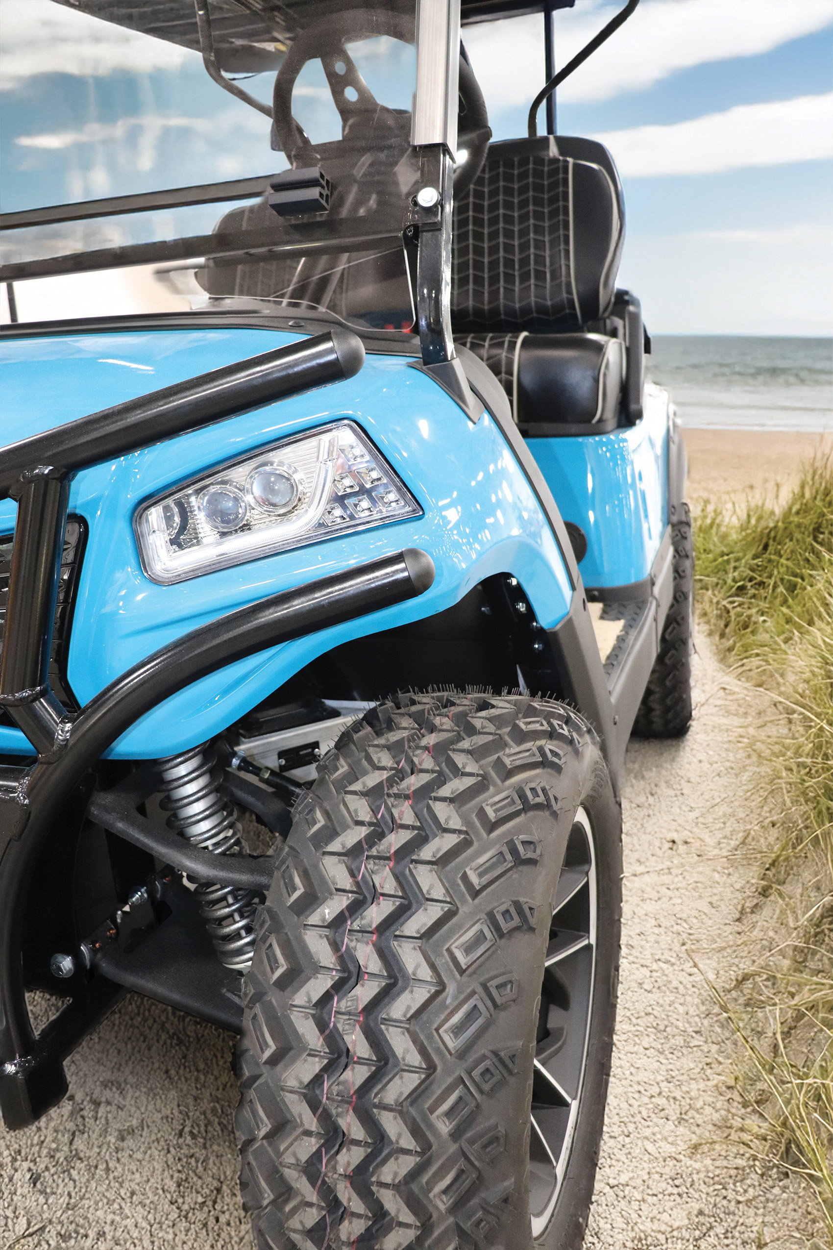 Blue Honor LUXE cart showing its front wheel, tire and suspension beside the beach